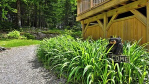 A wooden cabin with a 'WELCOME' sign, surrounded by lush greenery and a gravel path. - Fun In Fun Out Upper: 3BR with Two Decks, Sauna and Hot Tub (Killington)