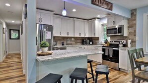 A modern kitchen with white cabinets, a stainless steel refrigerator, a microwave, and a built-in oven. There is a wooden island with a marble countertop and two black stools. - Fun In Fun Out Upper: 3BR with Two Decks, Sauna and Hot Tub (Killington)