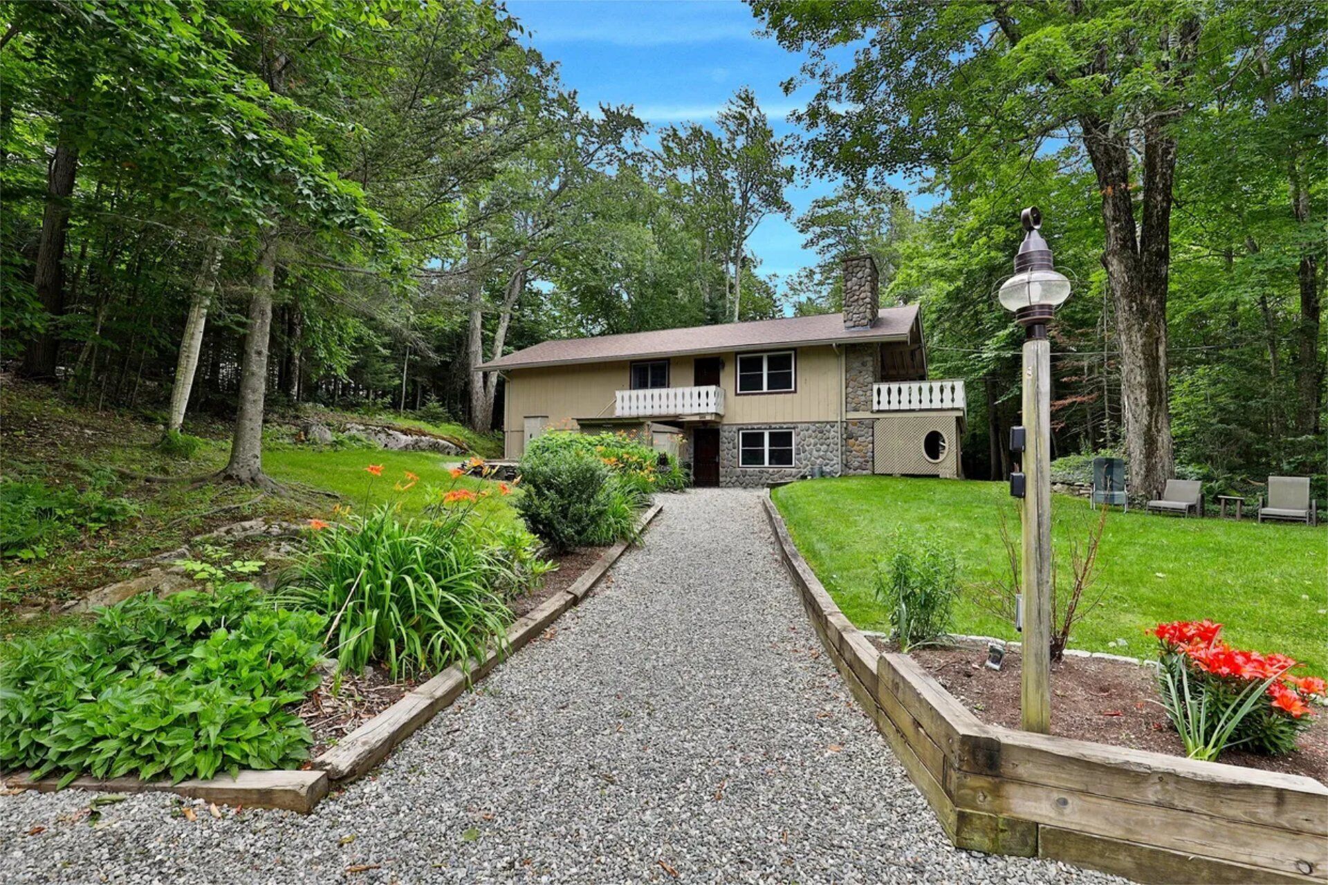 Summer exterior view of our ski home in Killington, Vermont. A beautiful large vacation home surrounded by trees, bushes and lawn, with large windows and outdoors decks.