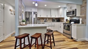 A modern kitchen with white cabinets, stainless steel appliances, a marble countertop, and wooden stools.