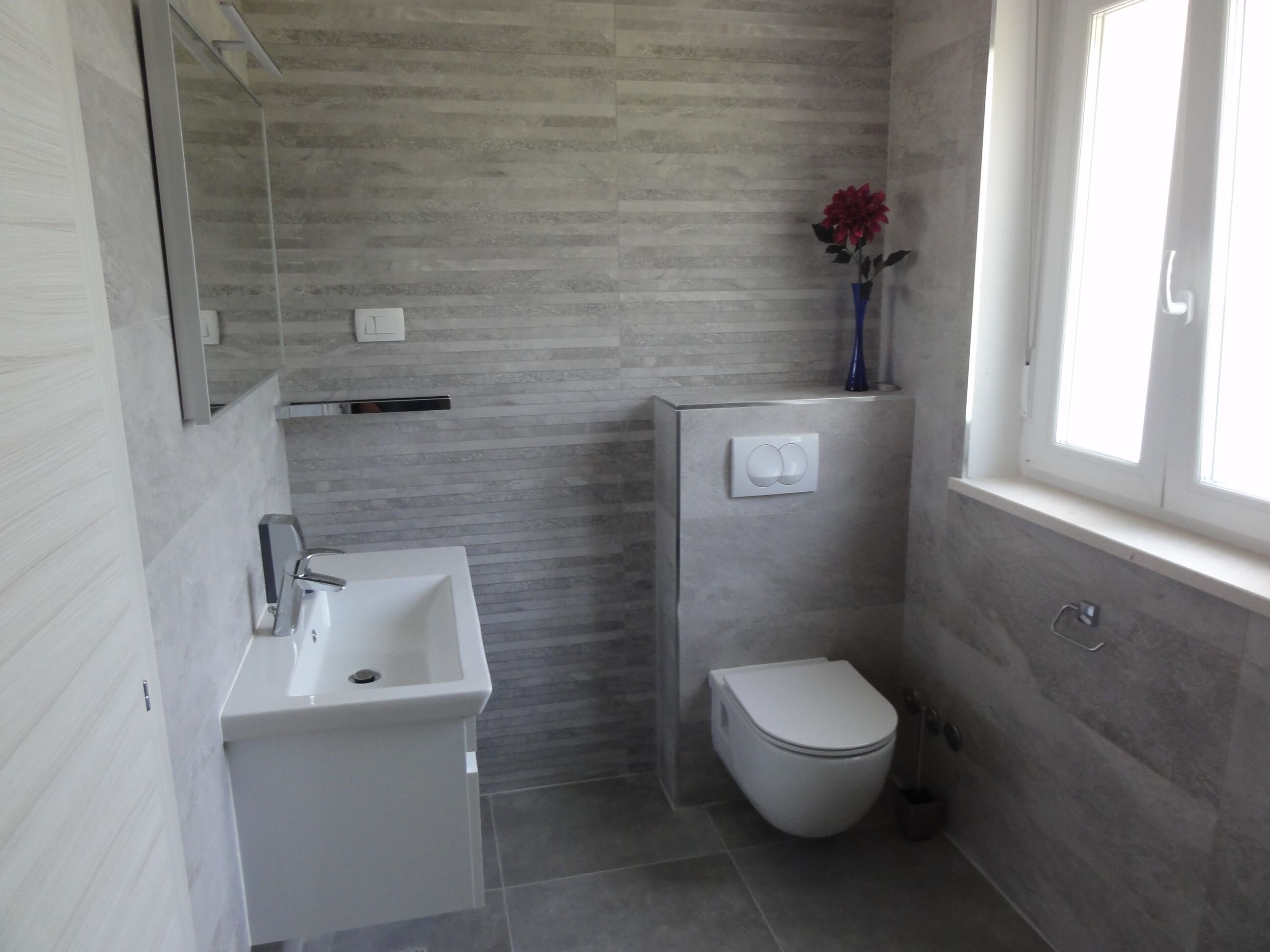 Un bagno compatto con lavandino, WC e interruttore della luce a parete.