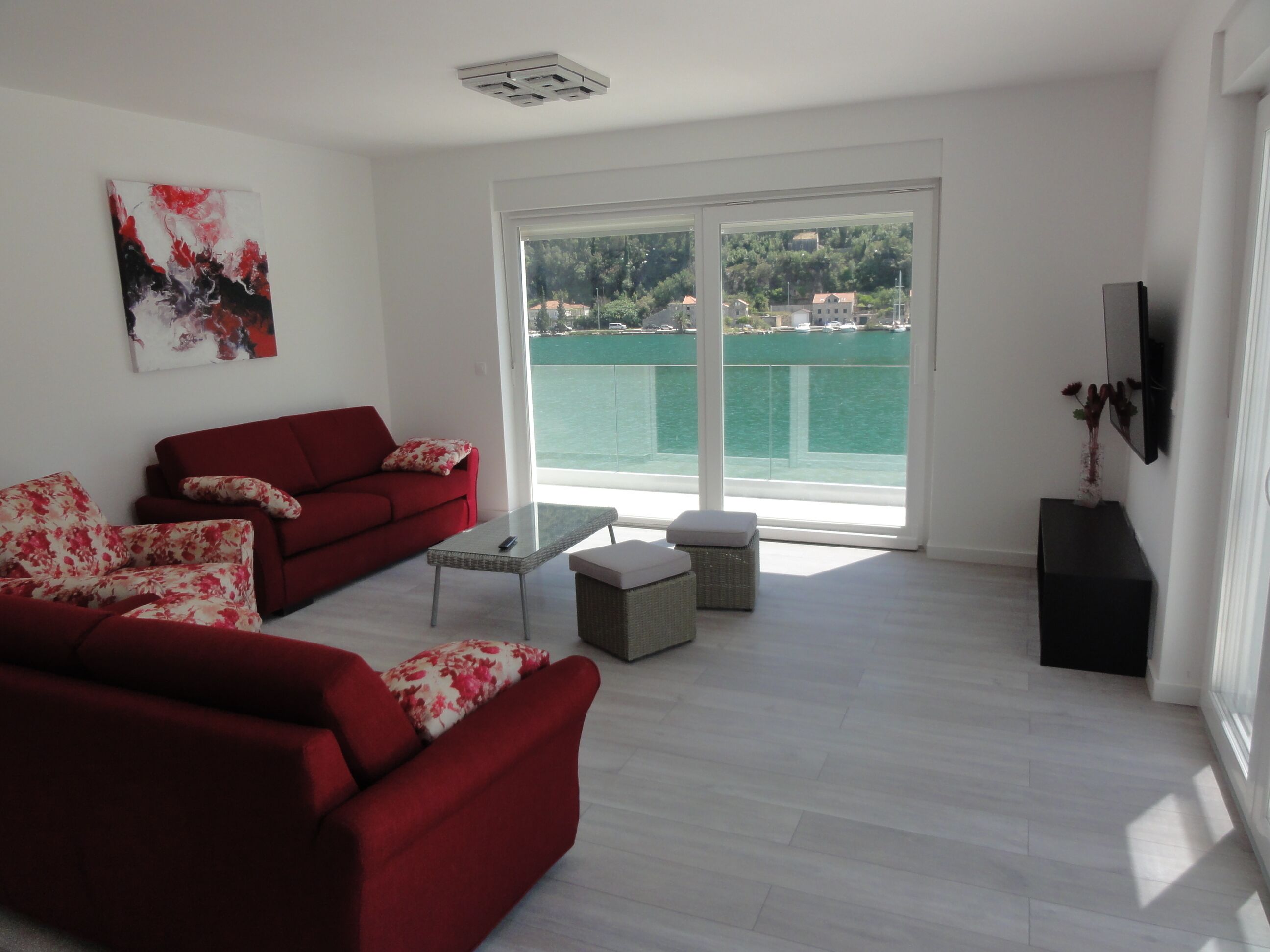 A modern living room with a red sofa, a glass coffee table, and a view of a body of water through large windows.