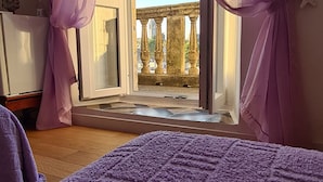 A room with a large window, a bed with a purple blanket, and a view of an outdoor balcony with columns. - Rooms Milena (Dubrovnik)