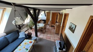 Ein gemütlicher Wohnbereich mit einer Couch, einem Tisch mit Blumenmuster-Tischdecke, einer Hängeleuchte und einem Blumentopf.