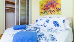 Un dormitorio con cama, un armario de puertas correderas y un cuadro abstracto y colorido en la pared.