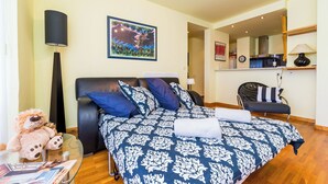 Un dormitorio con una cama, una silla, una lámpara, un oso de peluche y un cuadro en la pared.