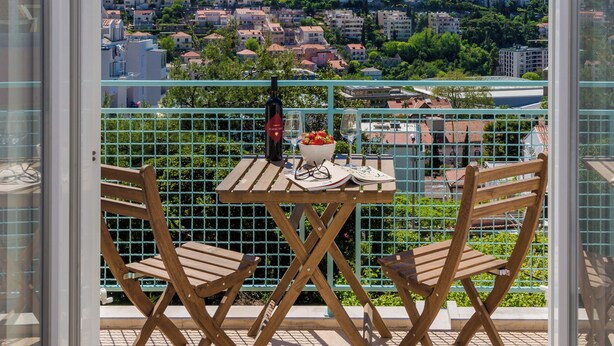 A balcony with a table and chairs, overlooking a residential area with buildings and greenery. - Apartments Terra (Dubrovnik)