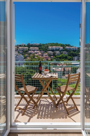 A balcony with a table and chairs, overlooking a residential area with buildings and greenery. - Apartments Terra (Dubrovnik)