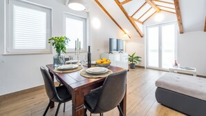 A dining area with a wooden table, chairs, and a bowl of lemons. There is a sofa and a TV in the background. - Apartments Terra (Dubrovnik)