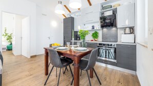 A modern kitchen with a dining area, featuring a wooden table, black chairs, and a built-in oven. - Apartments Terra (Dubrovnik)