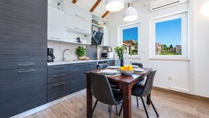 A modern kitchen with dark cabinetry, a dining table set for four, and a large window offering a view of the city. - Apartments Terra (Dubrovnik)