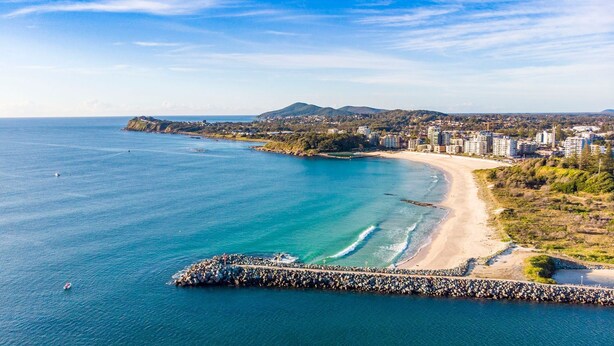 A coastal area with a rocky breakwater, a sandy beach, and a residential area with buildings. - Headlands 9 - Forster beachfront (Forster)