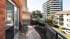 A balcony with a glass door, a small table, and chairs, overlooking a residential area with multi-story buildings. - Headlands 9 - Forster beachfront (Forster)