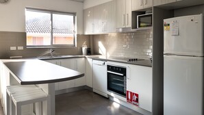 A modern kitchen with white cabinets, a built-in oven, and a refrigerator. - Headlands 9 - Forster beachfront (Forster)