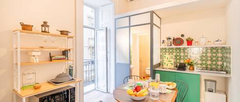 A compact living space with a dining area, kitchenette, and a sliding glass door leading to a balcony.