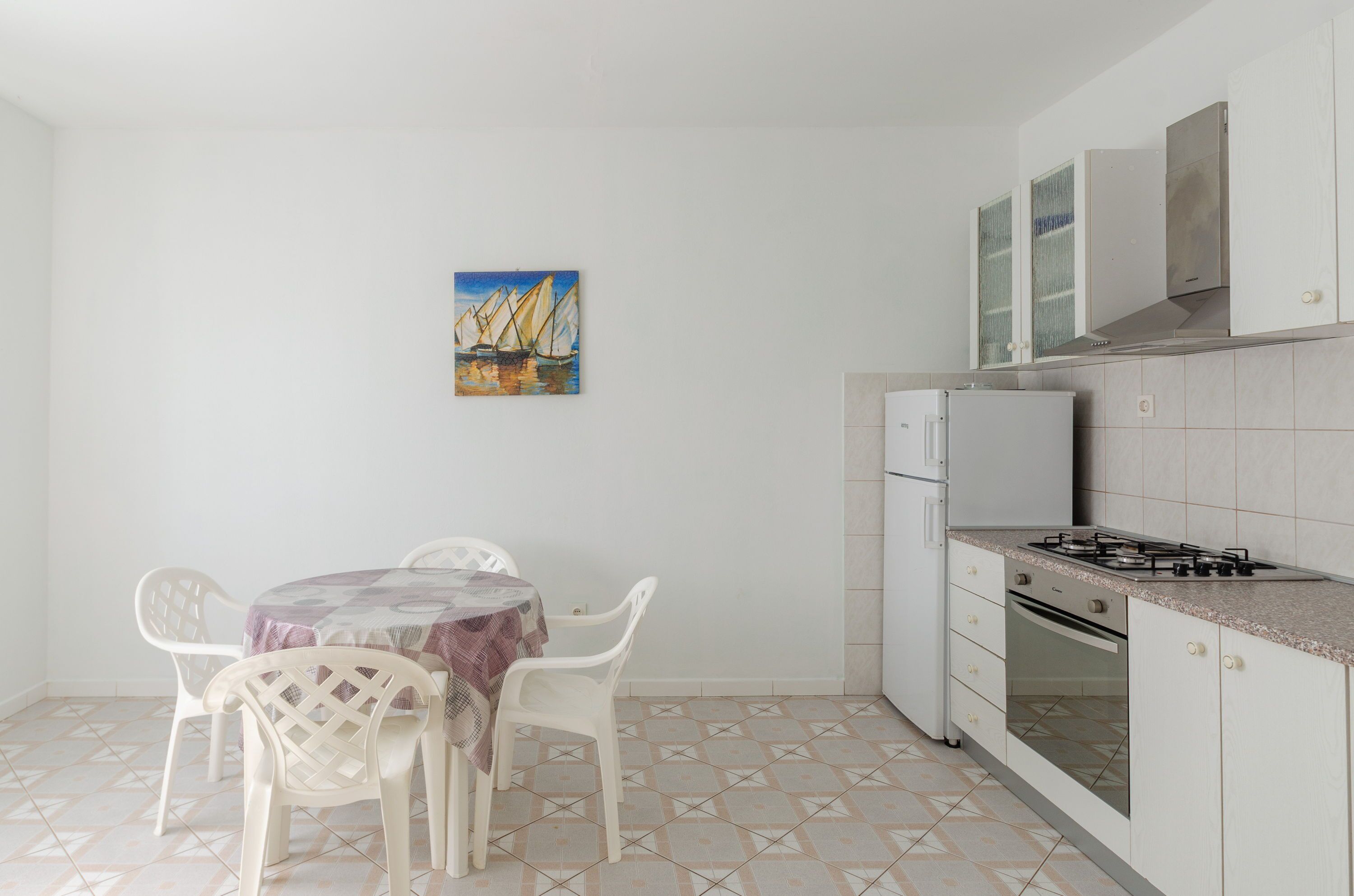 A compact kitchen with a dining table, chairs, a refrigerator, a stove, and a tiled backsplash.