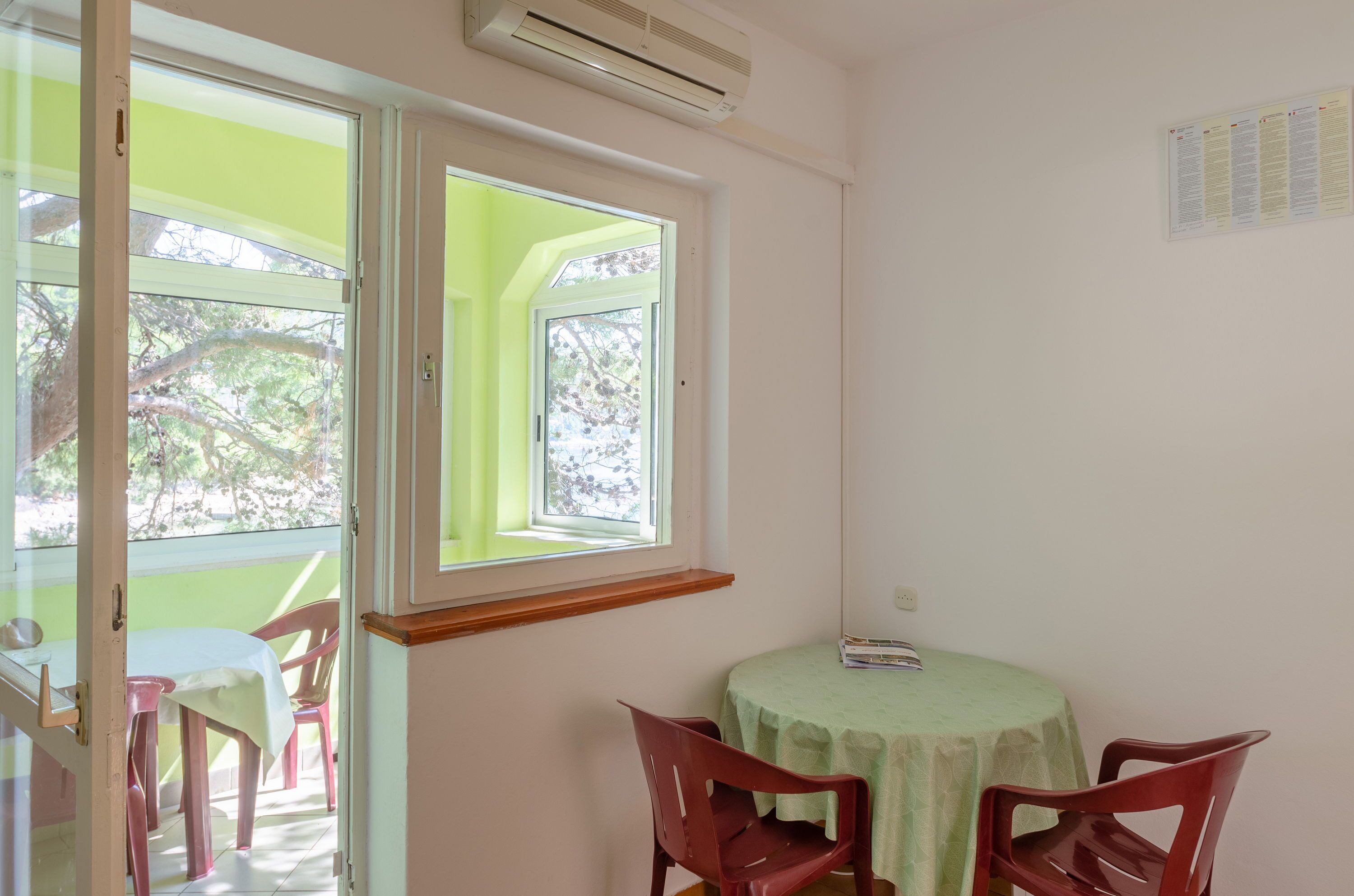 Una habitación con una mesa y sillas, una ventana con vistas a árboles, y un equipo de aire acondicionado en la pared.