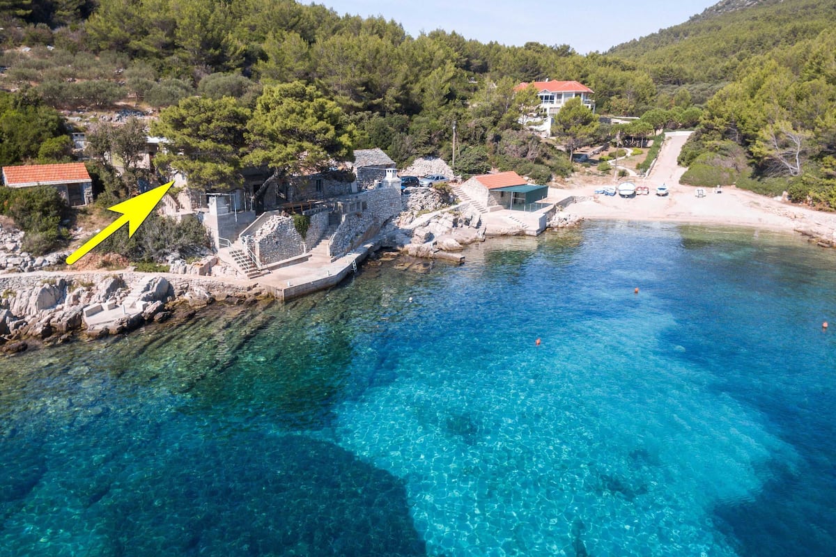 A coastal area with clear blue waters, a stone staircase leading down to the beach, and a building with a red roof.