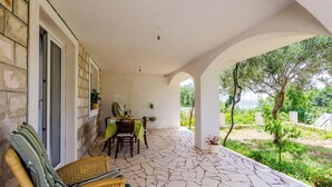 A covered outdoor seating area with a table and chairs, stone flooring, and a view of a garden. - Suite Room Little Rea (Zupa dubrovacka)