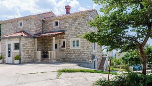 A two-story stone house with a tiled roof, a front porch, and a staircase leading to the entrance. - Suite Room Little Rea (Zupa dubrovacka)