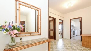 A hallway with a glass-top console table, a mirror, and a vase of flowers.