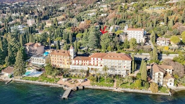 An aerial view of a coastal town with a prominent hotel featuring multiple floors, a swimming pool, and a dock extending into the water.