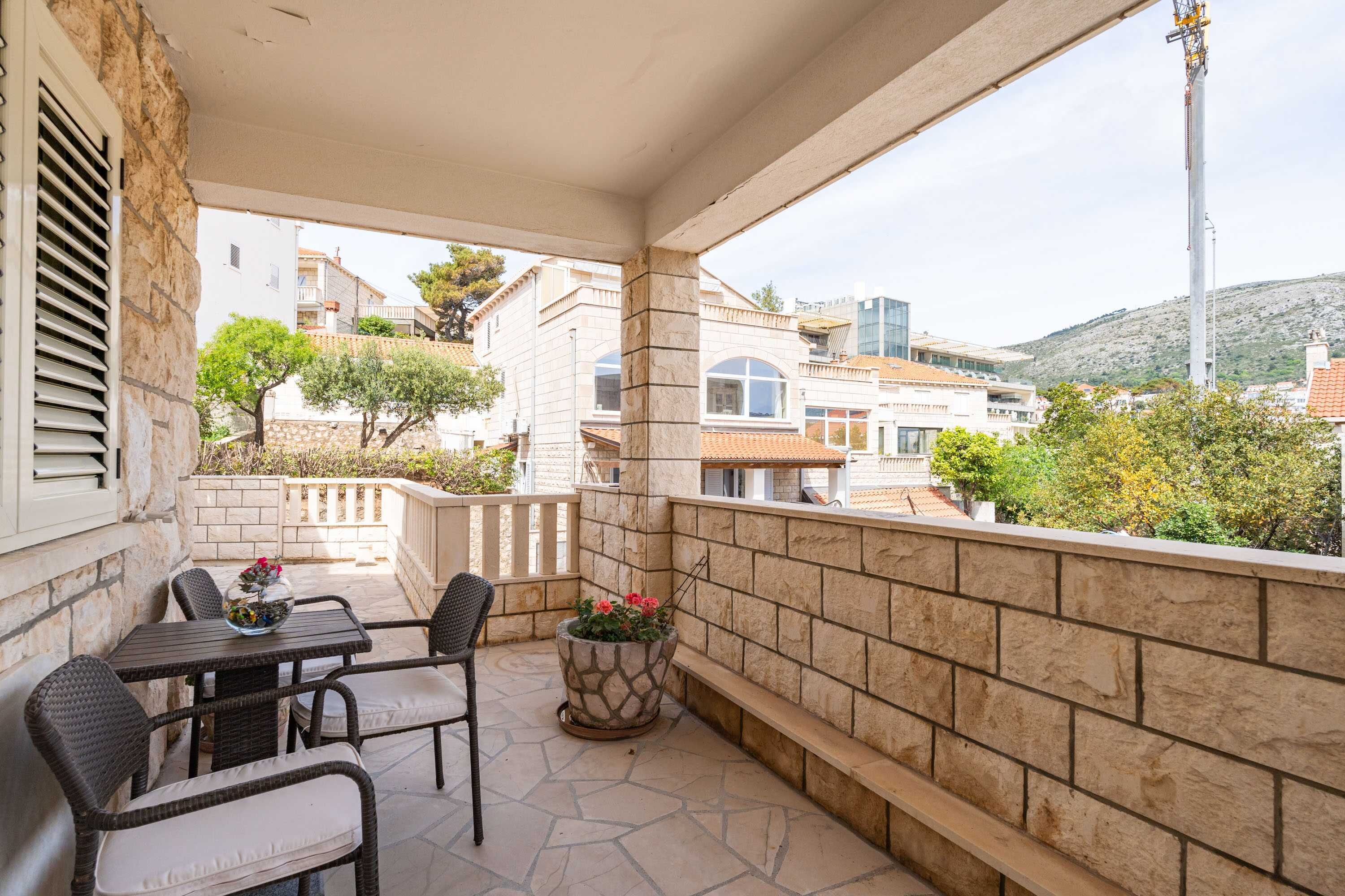 A balcony with stone walls, a table with chairs, and a potted plant.