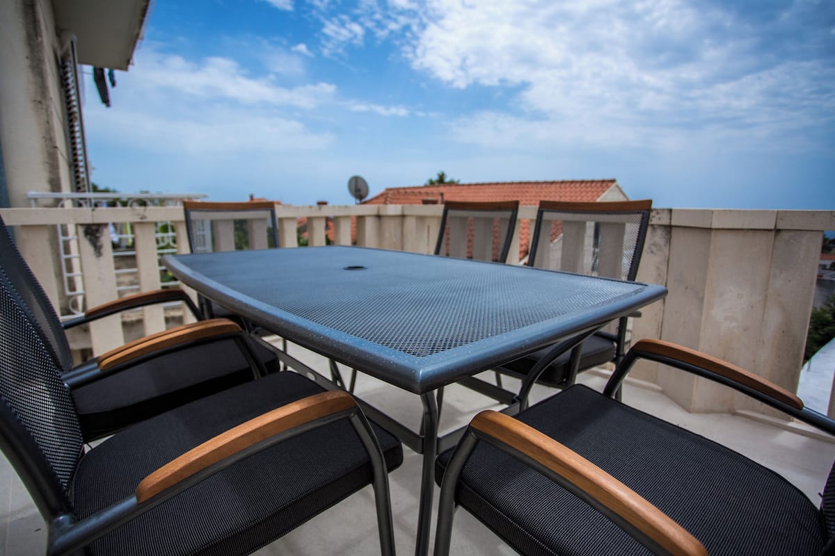 A balcony with a table and chairs, a view of buildings, and a clear sky.