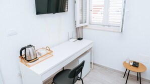 A small, white room with a desk, chair, and a small table with a kettle and a basket. - Serious Job Room (Dubrovnik)
