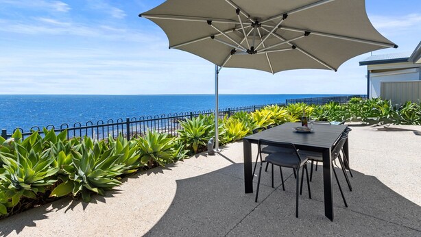 An outdoor patio with a table and chairs, a large umbrella, and a view of the ocean. - Sea La Vie - Absolute beachfront!  Amazing sea views! Off peak special! (Port Victoria)
