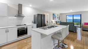 A modern kitchen with white cabinetry, a stainless steel range hood, and a built-in island with a sink. - Sea La Vie - Absolute beachfront!  Amazing sea views! Off peak special! (Port Victoria)
