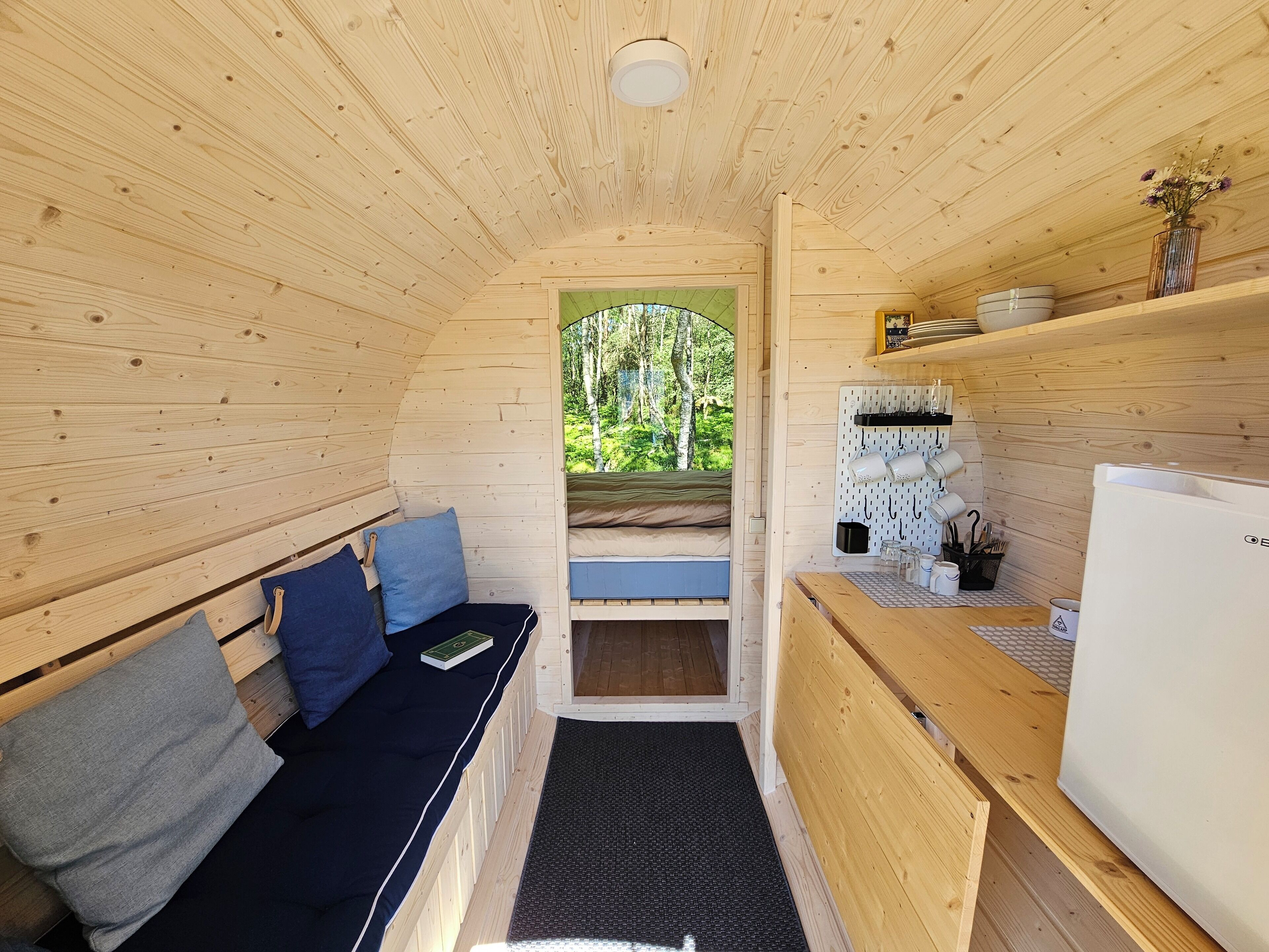 A cozy cabin interior with a wooden bench, a small table, and a refrigerator.