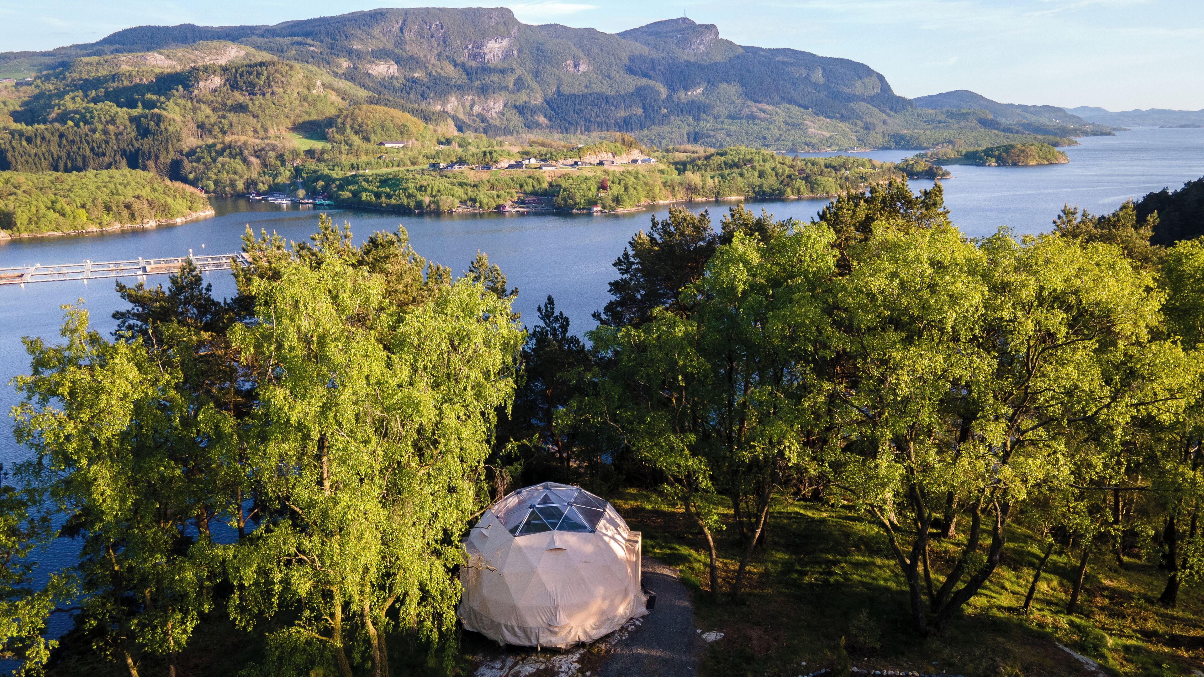 A dome tent in a forested area with a lake and mountains in the background.