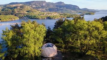 A dome tent in a forested area with a lake and mountains in the background.