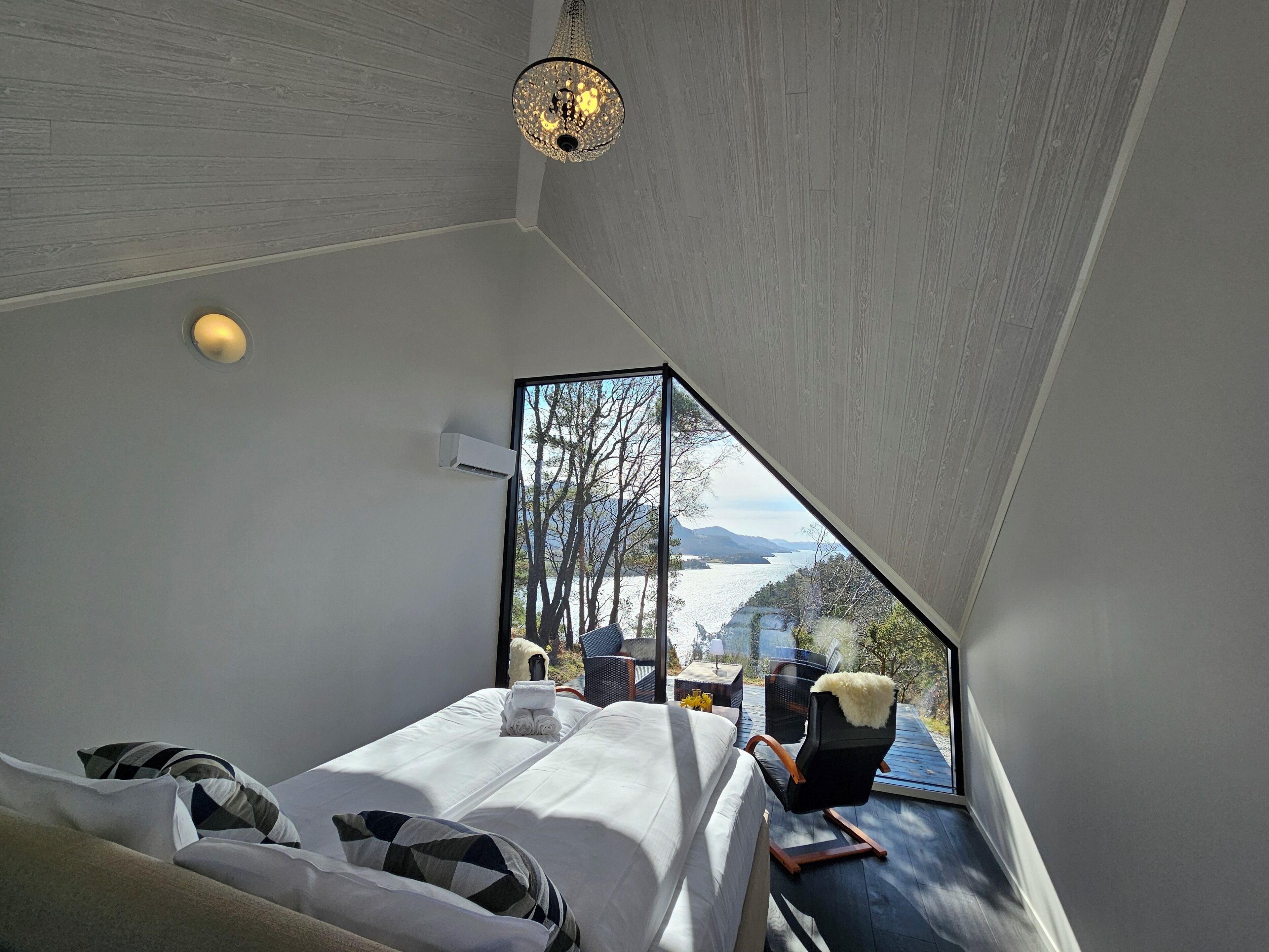 A bedroom with a large window, a bed, a chair, and a hanging light fixture.