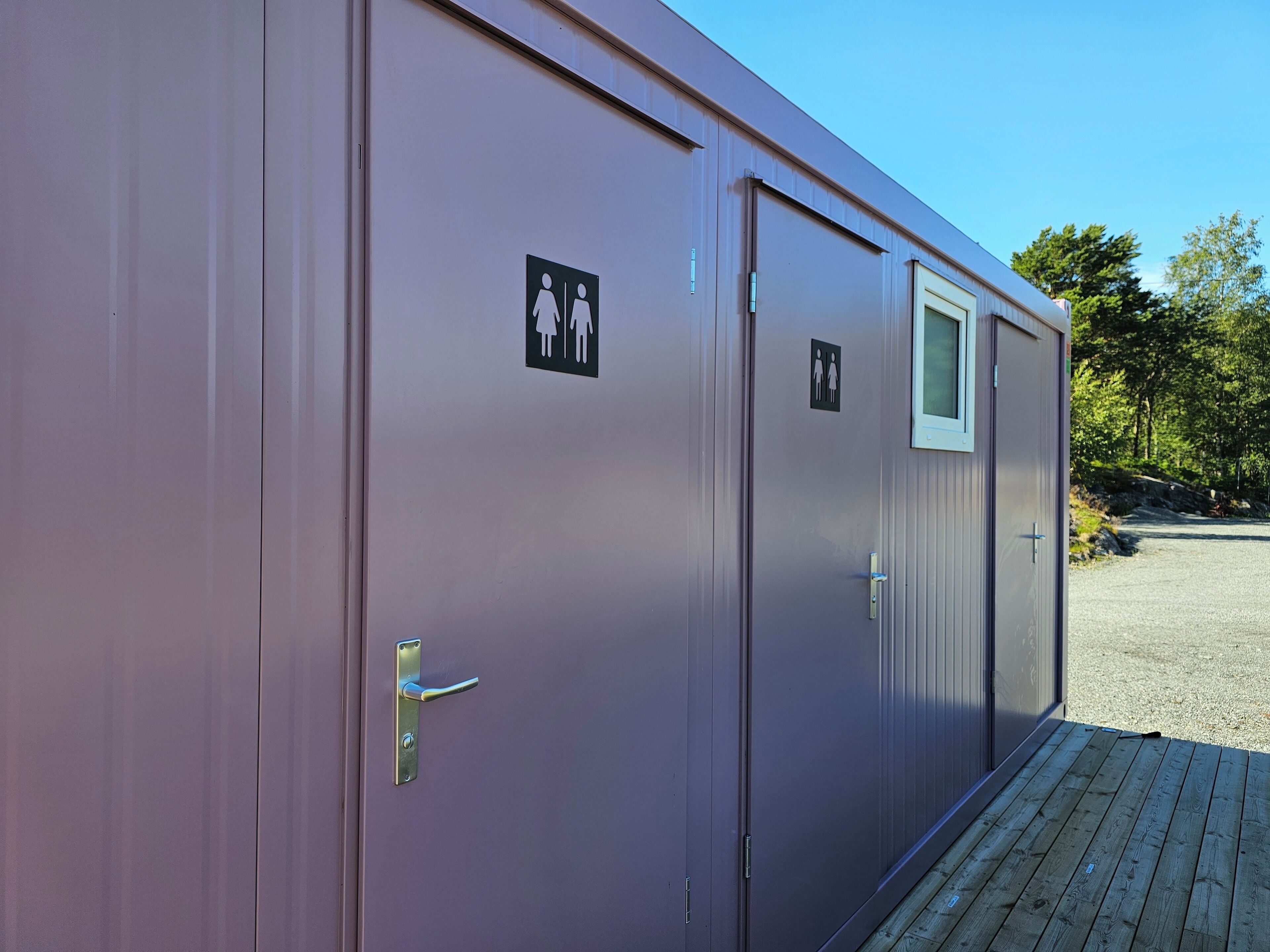 A row of two-room portable cabins with exterior doors and windows, each marked with a gender-specific restroom symbol.