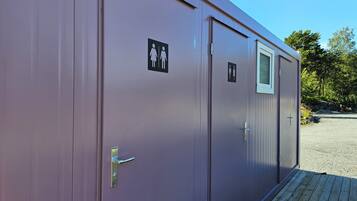 A row of two-room portable cabins with exterior doors and windows, each marked with a gender-specific restroom symbol.