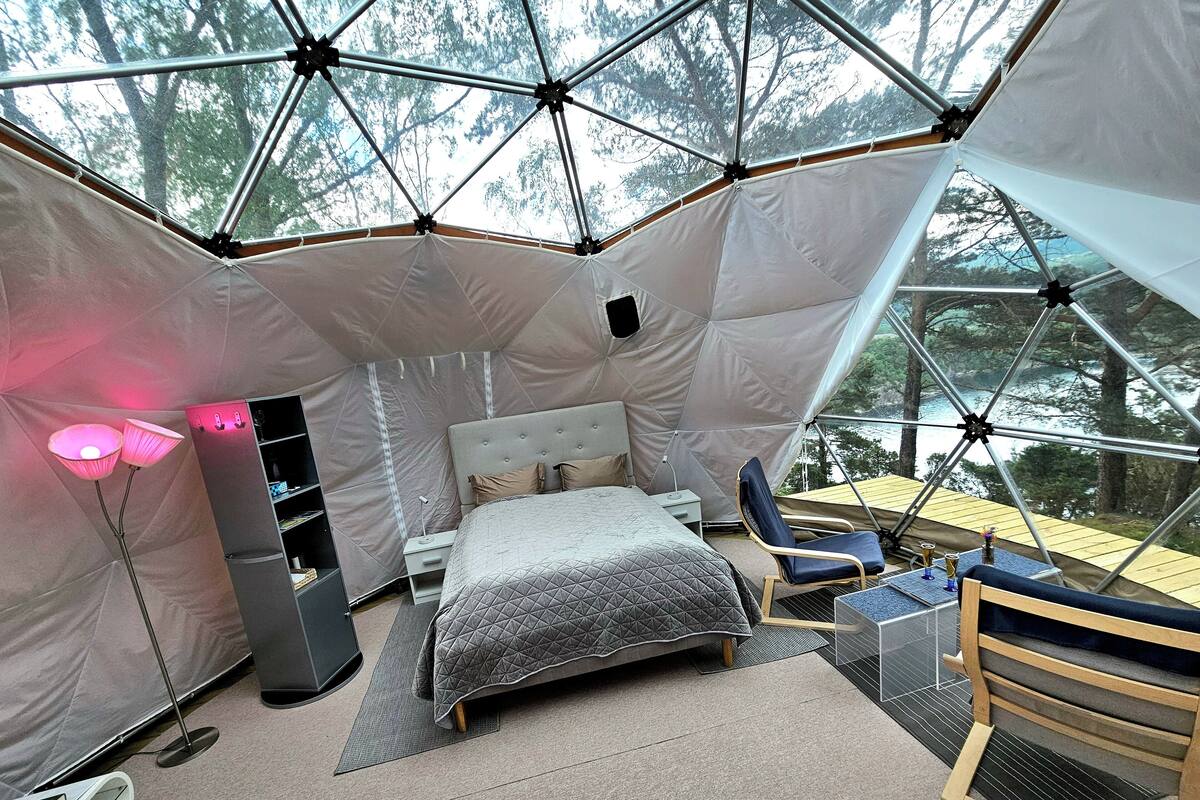 A tented accommodation with a bed, seating area, and a view of the forest.