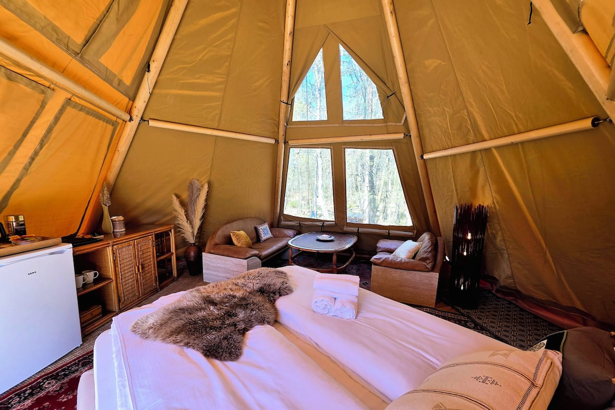 A tent interior with a bed, a small table, a sofa, and a window.