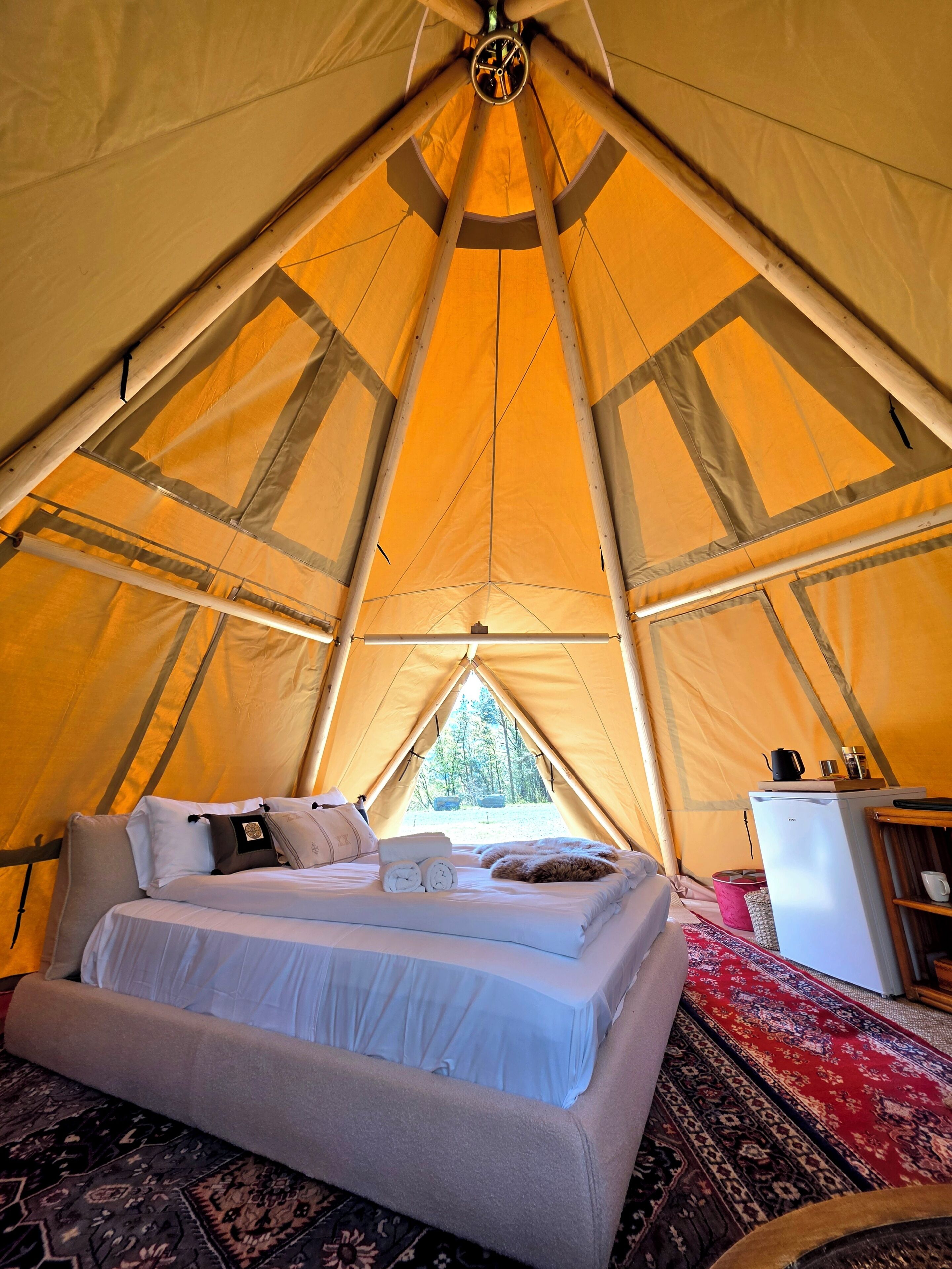 A tent with a bed, a small refrigerator, and a window.