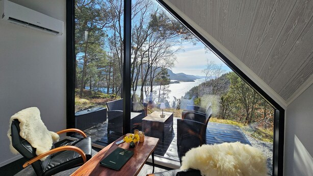 A modern room with a large glass window, a wooden table, two chairs, and a fur throw. - NorGlamp (Hjelmeland)