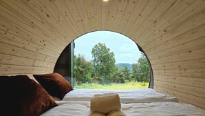 A cozy room with a large arched window, wooden walls, a bed with white linens, and a brown pillow. - NorGlamp (Hjelmeland)