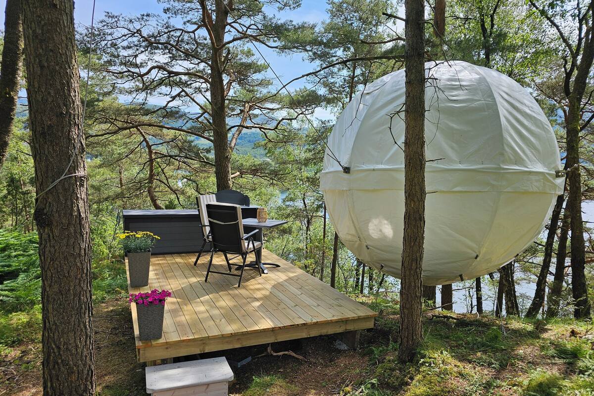 A large dome tent in a forested area with a deck, chairs, and a table.