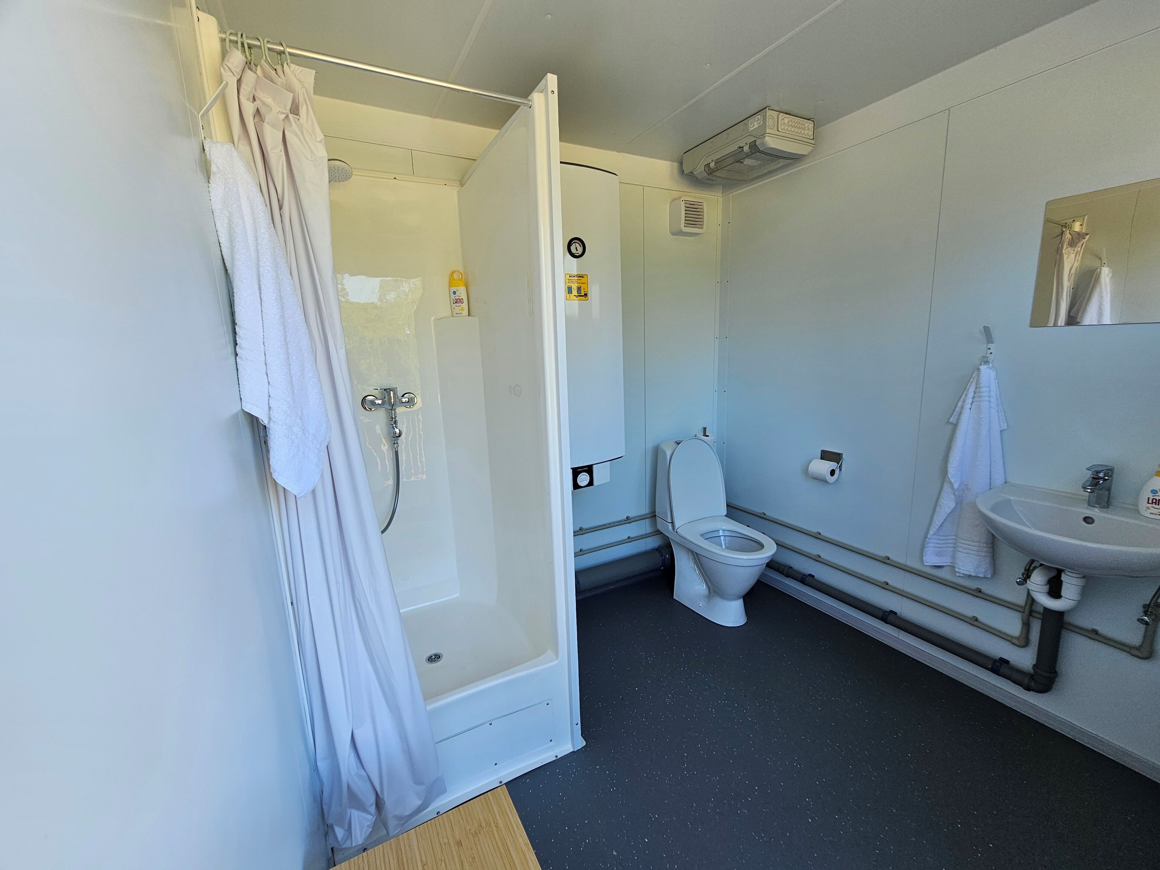 A bathroom with a shower, toilet, sink, and a mirror.