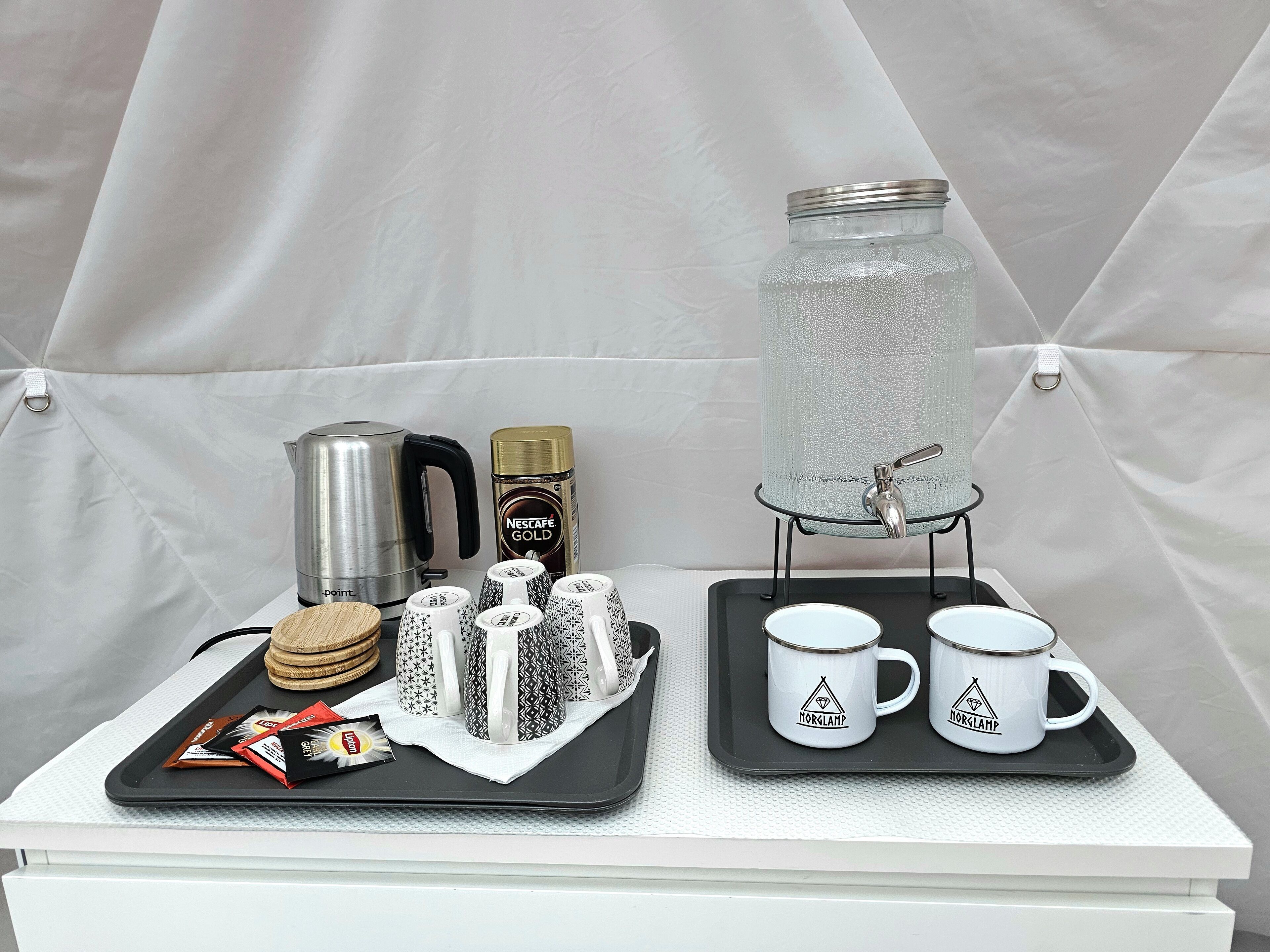 Ein Tablett mit einer Nescafe Gold Kaffeemaschine, einem Wasserspender und zwei Tassen mit dem Norclamp-Logo.