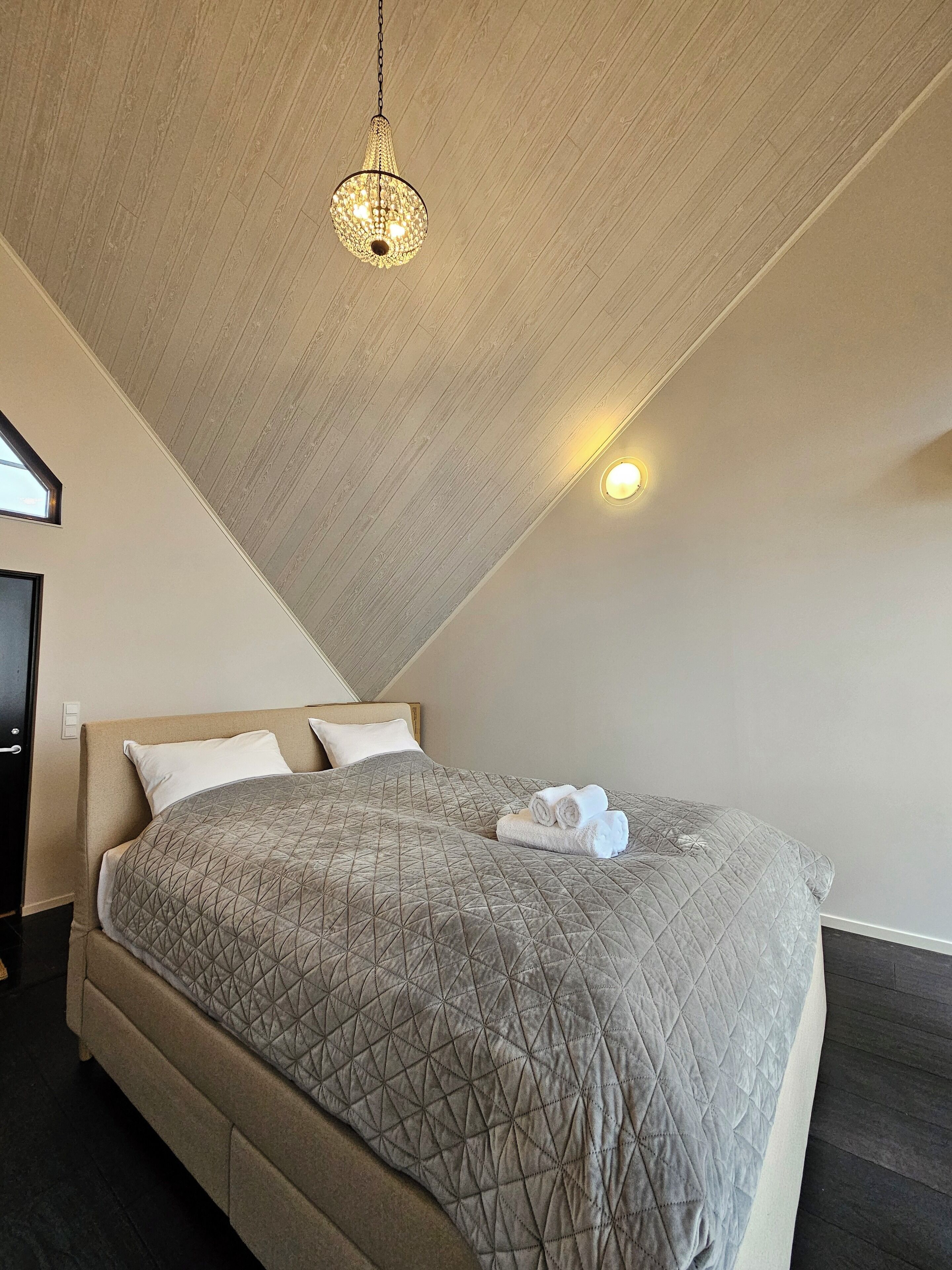 A bedroom with a large bed, a hanging light fixture, and a small wall-mounted light.