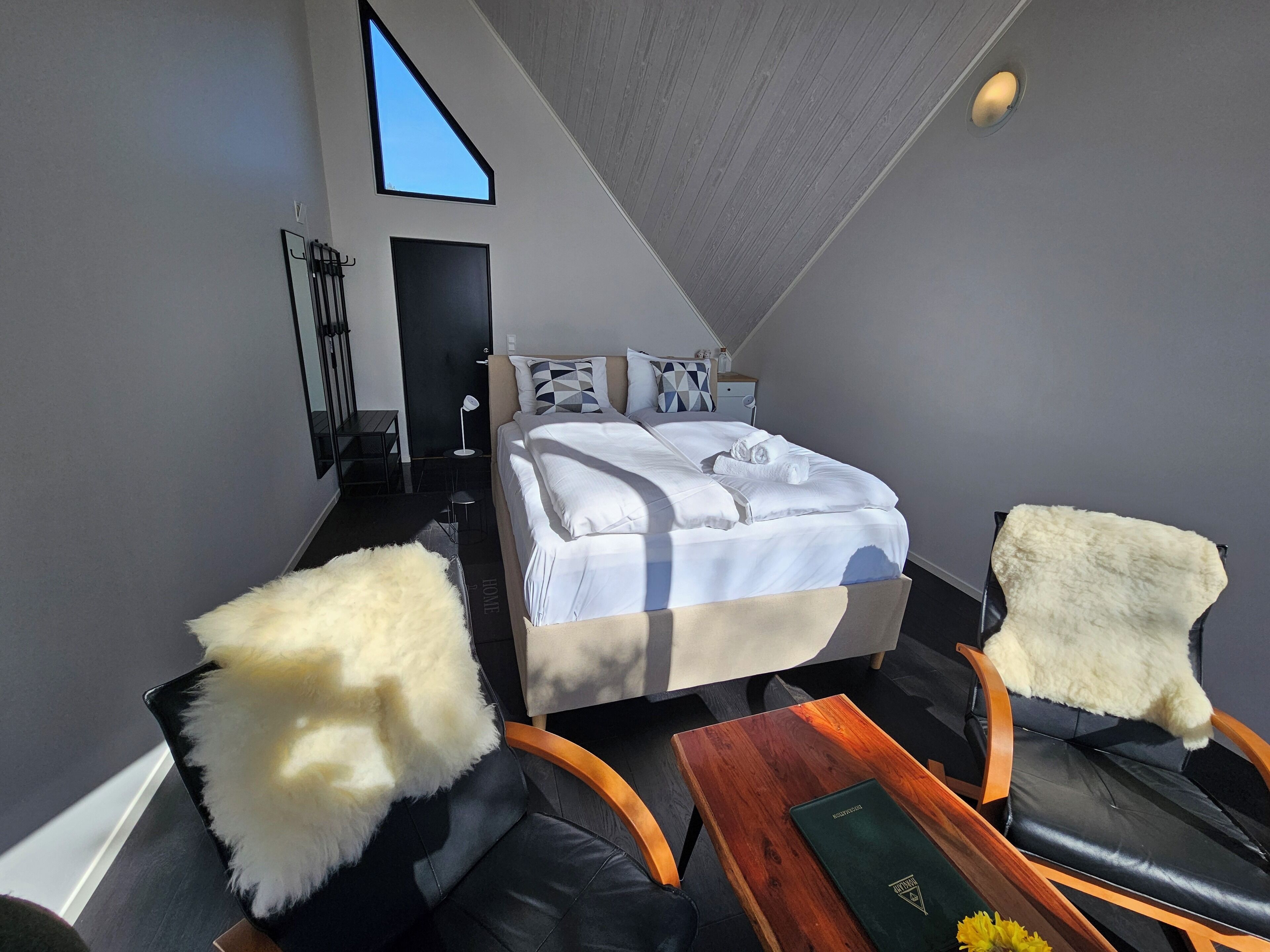 A modern hotel room with a large bed, a desk, a chair, and a small table.