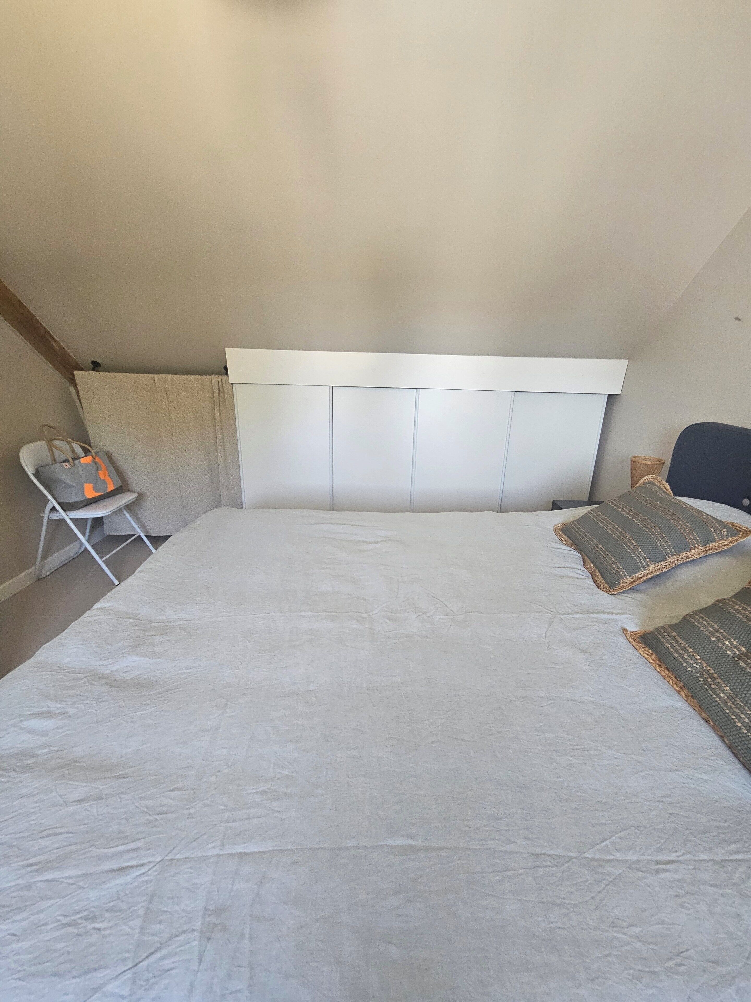 A bedroom with a large bed, a headboard, a chair, and a small table.