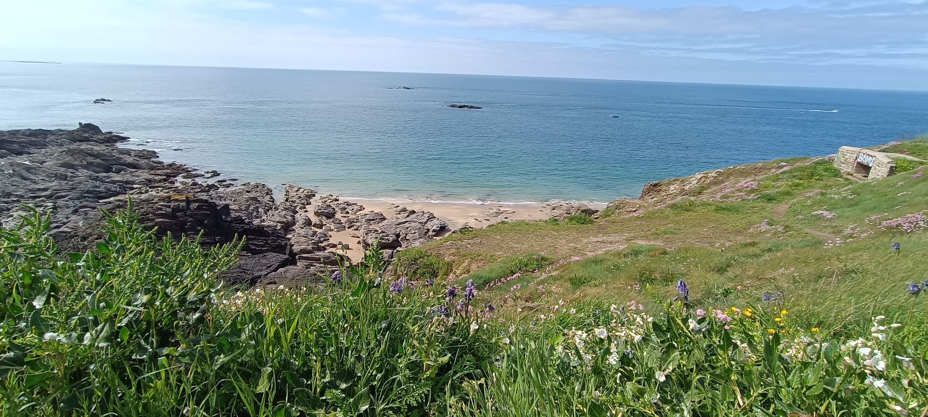 A coastal landscape with rocky terrain, a sandy beach, and a clear view of the sea.
