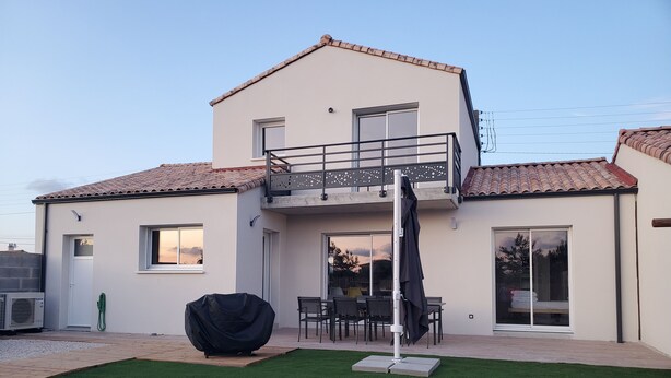 Ein zweistöckiges Haus mit Balkon, einer Terrasse, einem Tisch und Stühlen sowie einem überdachten Grill.